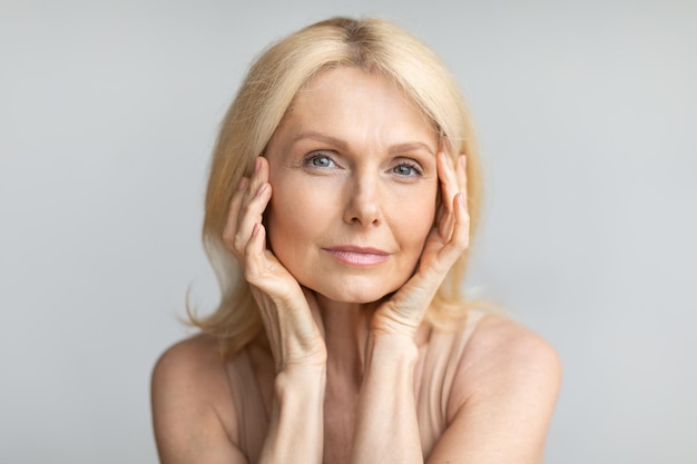 Portrait of beautiful mature blonde woman touching her face posing looking and smiling at camera