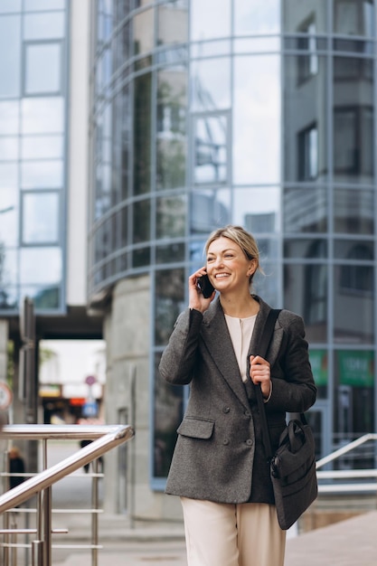 Portrait of a beautiful mature business woman in suit and gray jacket smiling and talking on the phone on the modern urban background