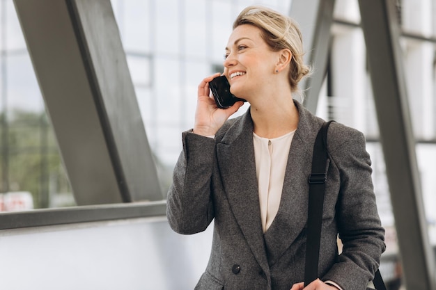 Portrait of a beautiful mature business woman in suit and gray jacket smiling and talking on the phone on the modern urban background