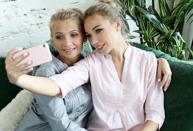 Portrait of beautiful mature mother and her daughter making a selfie using smart phone and smiling home and happy