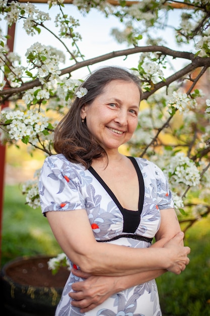 Portrait of beautiful mature woman in light dress against background of spring blooming gardens