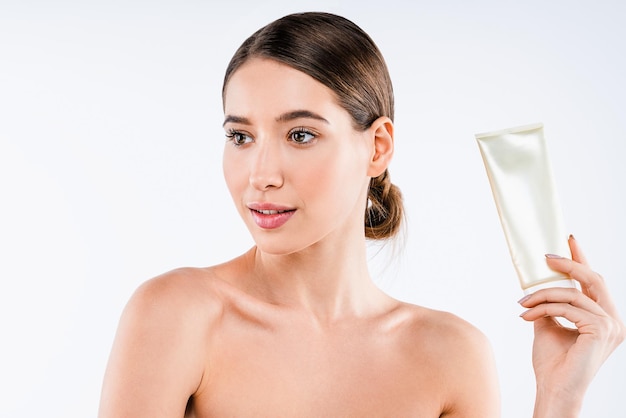 Portrait of beautiful model with shiny clean skin holding tube of cream isolated on white background