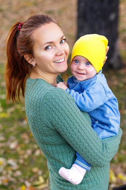 Portrait of beautiful mom holding on hands her baby in autumn park