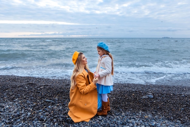 Portrait of a beautiful mother and daughter in warm clothes on the seashore in the cold season family walk along the beach