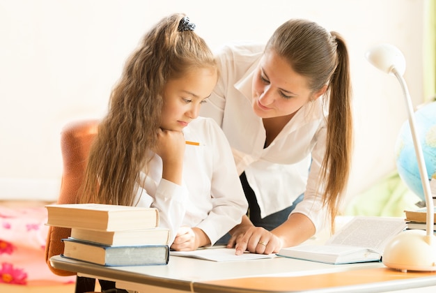 Portrait of beautiful mother helping daughter doing homework