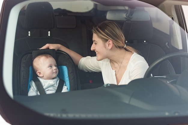 Portrait of beautiful mother at her baby sitting in child seat at car