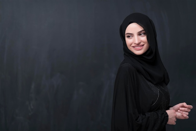 現代のイスラムファッションとラマダン・カリームのコンセプトを表す黒い黒板の前にヒジャーブを着たファッショナブルなドレスを着た美しいイスラム教徒の女性のポートレート。