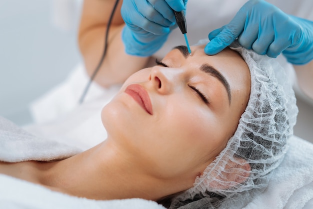 Portrait of a beautiful nice woman lying with closed eyes while having a dermatology procedure