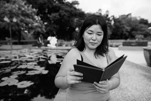 Portrait of beautiful overweight Asian woman relaxing at the park in the city in black and white