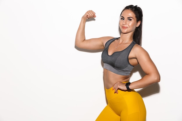 Portrait of beautiful pleased amazing young sports fitness woman isolated over white wall wall showing biceps.