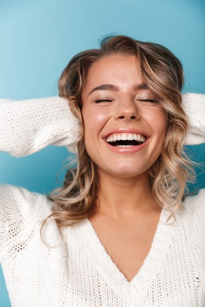 Portrait of beautiful pleased woman in white sweater laughing and grabbing her head