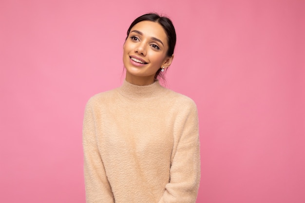 Portrait of beautiful positive cheerful cute smiling young brunette woman in casual beige sweater isolated on pink background with copy space.