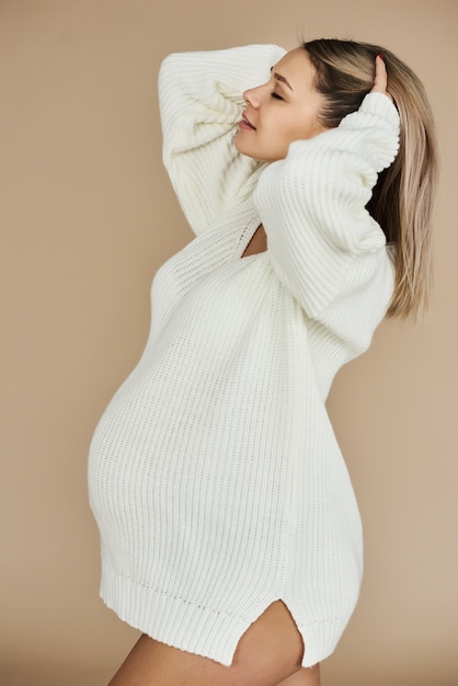 Foto un ritratto di una bella ragazza incinta vestita in maglione bianco in uno sfondo beige.