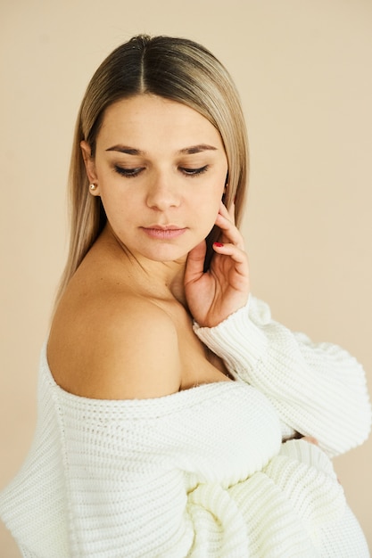 Un ritratto di una bella ragazza incinta vestita di maglione bianco in uno sfondo beige