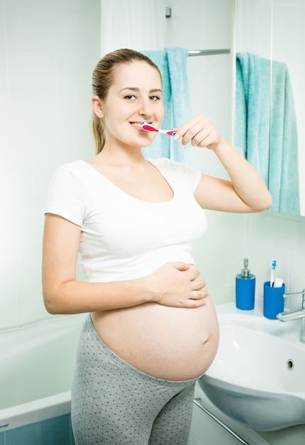 Portrait of beautiful pregnant woman brushing teeth in bathroom at morning