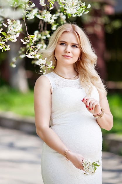 Portrait of beautiful pregnant woman in the flowering park. Young happy pregnant woman enjoying life in nature.