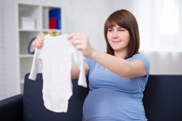 Portrait of beautiful pregnant woman looking at baby's clothes