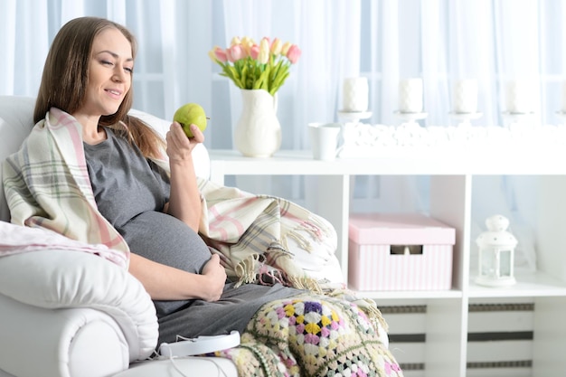 Portrait of beautiful pregnant woman sitting in armchair with apple