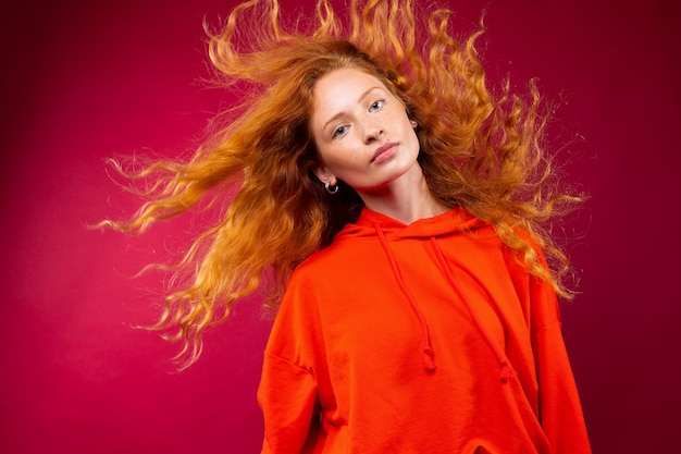 Portrait of a beautiful red-haired girl with flying curly hair on a red wall.