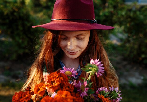 Portrait of a beautiful redhaired teenage girl in a red hat holding a bouquet of flowers