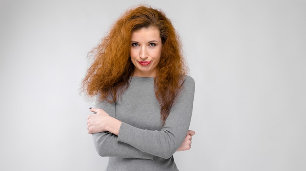 Portrait of beautiful redhead unhappy young woman in gray clothes on gray background