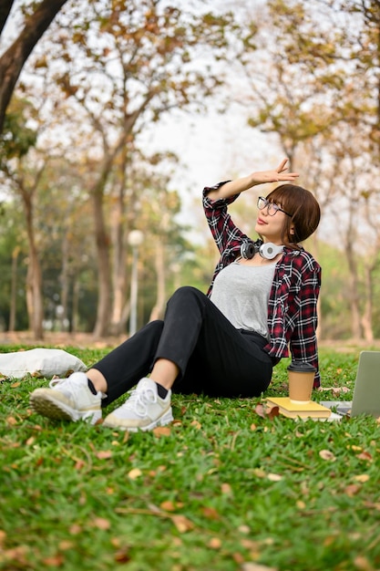 緑豊かな公園の芝生の上に座っている、美しくリラックスしたアジアの若い女性のポートレート