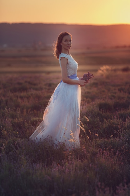 Portrait of beautiful romantic woman in fairy field of lavender with bouquet