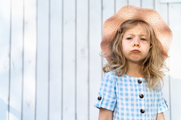 Portrait of a beautiful sad little girl with blond curly hair in a hat.