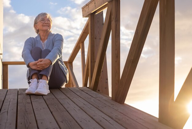 Portrait of beautiful senior woman in blue sitting outdoors in sunset light looking at the horizon