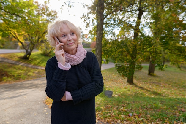 Portrait of beautiful senior woman with short blond hair relaxing at the park outdoors in autumn