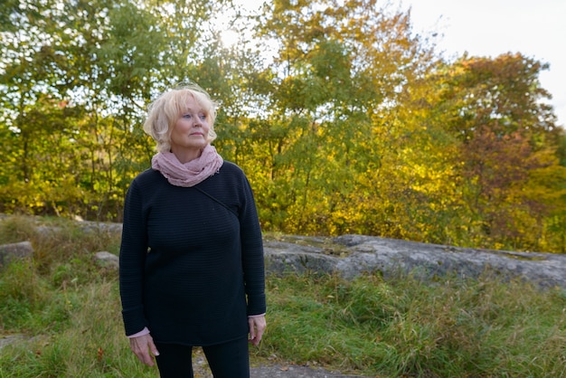 Portrait of beautiful senior woman with short blond hair relaxing at the park outdoors in autumn