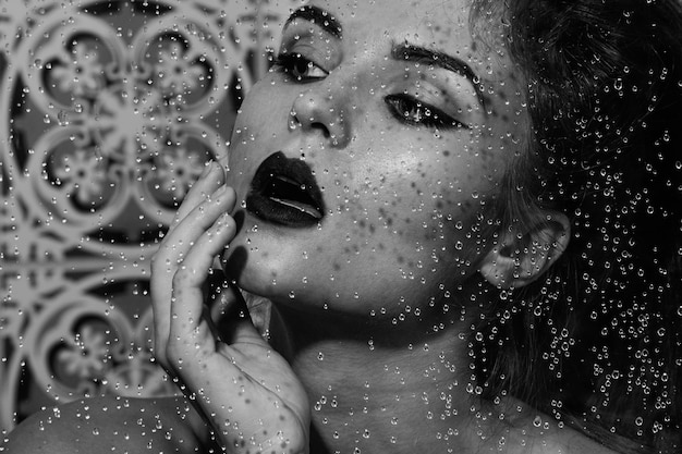 Portrait of beautiful and sensual woman captured through wet glass