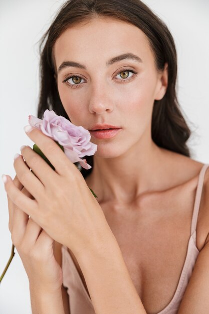 Ritratto di una bella giovane donna bruna sensuale che indossa un costume da bagno isolato, con in mano un fiore di rosa