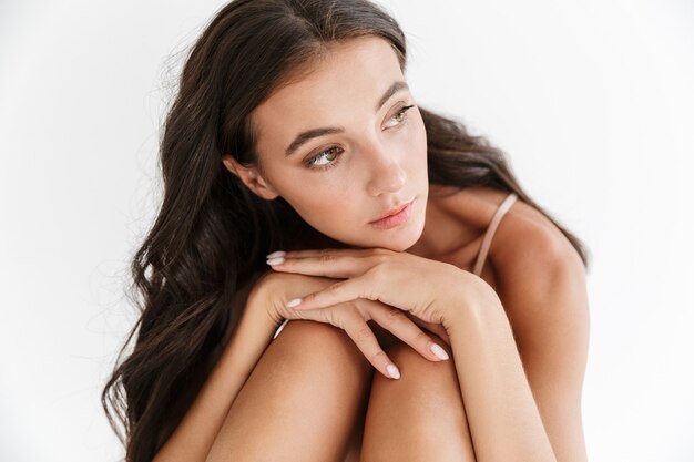 Portrait of a beautiful sensual young brunette woman wearing swimsuit sitting isolated, posing