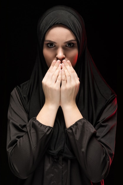 Portrait of beautiful serious young muslim woman wearing black hijab with hands near her face as praying concept