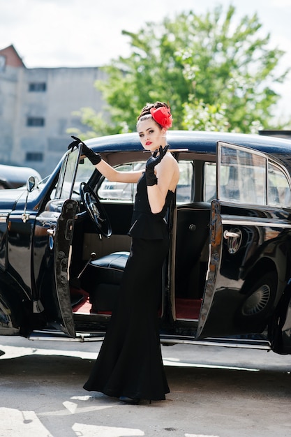 Portrait of beautiful sexy brunette fashion girl model with bright makeup in retro style near vintage car with a cigarette in hand.