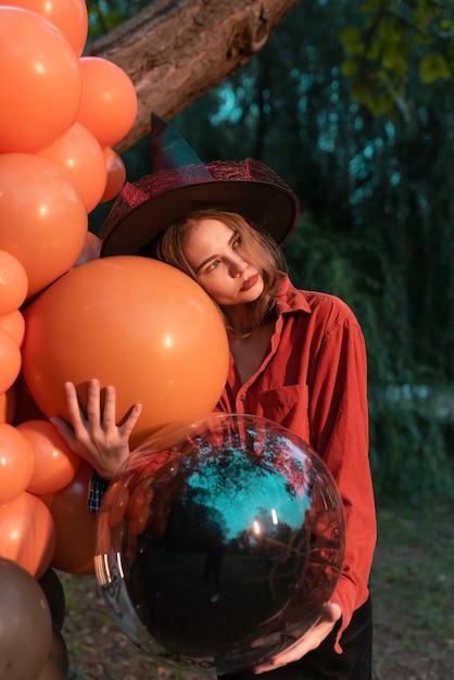 Portrait of beautiful sexy young woman in witch halloween costume with orange and black balloons