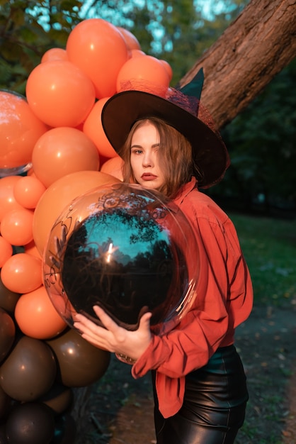 Портрет красивой сексуальной молодой женщины в костюме ведьмы на хэллоуин с оранжевыми и черными воздушными шарами