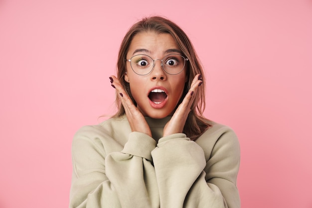 Photo portrait of beautiful shocked woman in eyeglasses isolated on pink