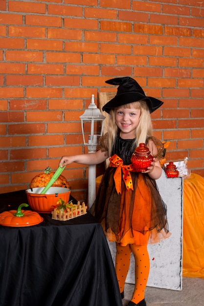 Foto ritratto di bella ragazza piccola in costume strega halloween arancione nero con la scopa. felice concetto di halloween. dolcetto o scherzetto. festa per bambini divertenti, infanzia felice.