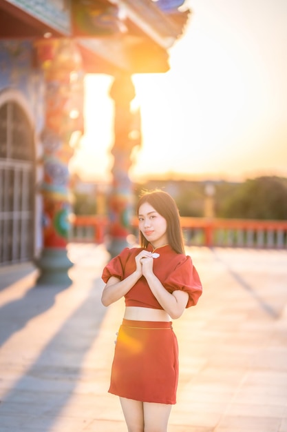 Portrait beautiful smiles Asian young woman wearing red cheongsam dress traditional decoration for Chinese new year festival celebrate culture of china at Chinese shrine Public places in Thailand