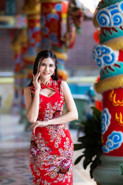 중국 새해 축제를 위해 빨간 치파오 드레스를 입은 아시아 젊은 여성이 태국의 중국 신사에서 중국 문화를 축하하는 아름다운 미소를 짓고 있습니다.