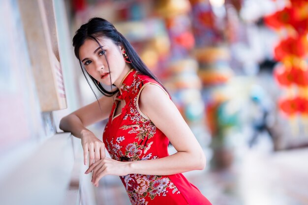 Ritratto bei sorrisi giovane donna asiatica che indossa cheongsam cinese tradizionale rosso, per la festa del capodanno cinese al santuario cinese