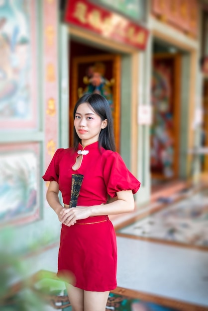붉은 중국 전통 치파오 장식을 입고 태국의 중국 신사에서 중국 신년 축제를 위해 중국 패닝을 들고 아름다운 미소를 짓는 아시아 젊은 여성