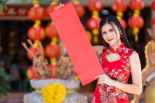 Portrait beautiful smiles asian young woman wearing red
traditional chinese cheongsam, holding show blank spring paper red
for chinese new year festival at chinese shrine