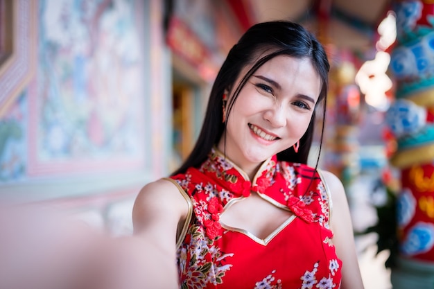 Портрет красивые улыбки азиатской молодой женщины в красном традиционном китайском чонсаме, делающей селфи со смартфоном на фестиваль китайского нового года в китайском храме