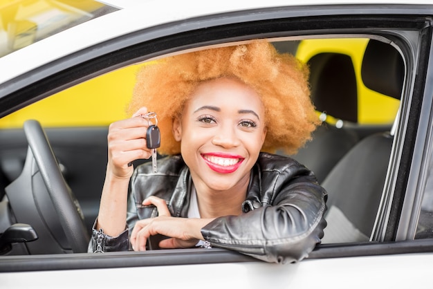 Portrait of a beautiful smiling african woman in leather jacket showing keys in the car on the yellow background