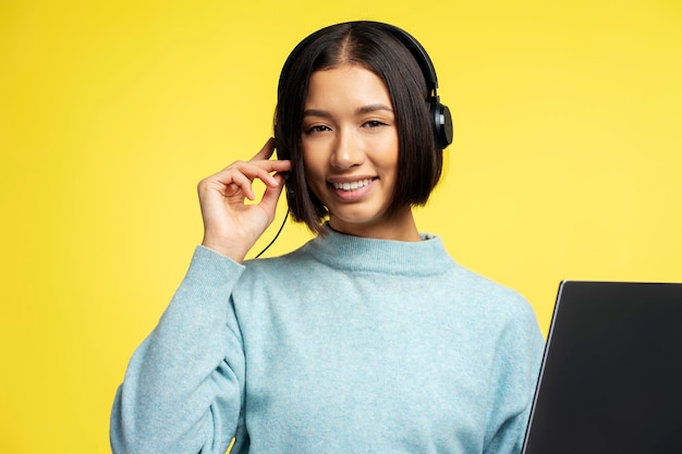 Foto ritratto di una bella donna asiatica sorridente operatrice di un call center che indossa le cuffie e guarda la telecamera una giovane impiegata che posa isolata su uno sfondo giallo comunicazione online