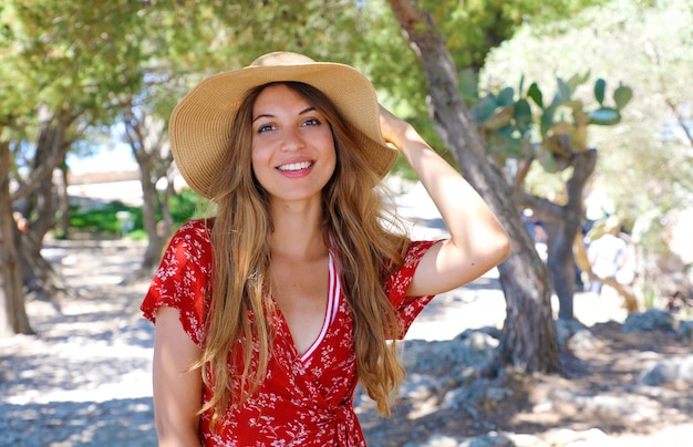 Portrait of a beautiful smiling girl wearing hat and red dress looking at camera outdoors