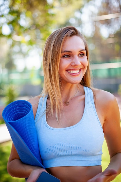 Portrait of a beautiful smiling happy woman in blue sportswear holding a yoga mat Healthy lifestyle and self body care concept